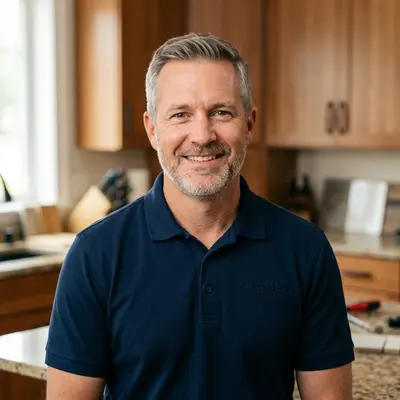 John Armstrong, owner of Kitchen Remodeling Mankato, smiling in a navy polo shirt with kitchen cabinets and granite countertops in the background